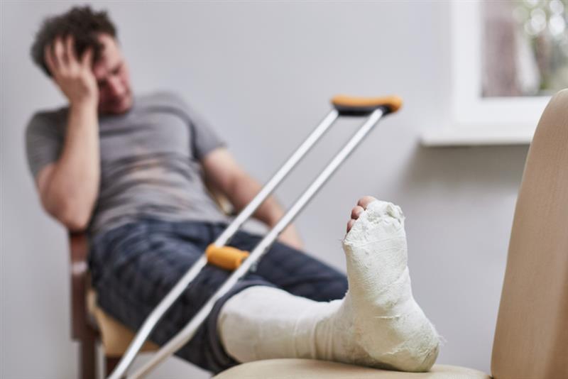 A man with a broken leg and crutches sits grabbing his head.