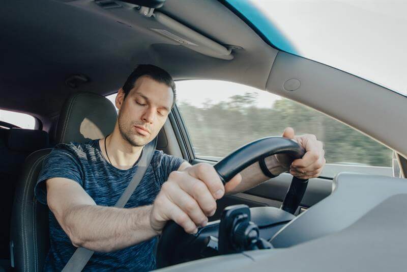 Fatigue of sleeping driver driving at speed while holding wheel while driving on highway in forest.