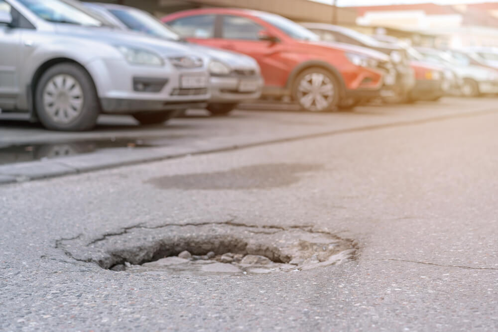 Big pothole with water after rain on asphalt road with car parking lot.