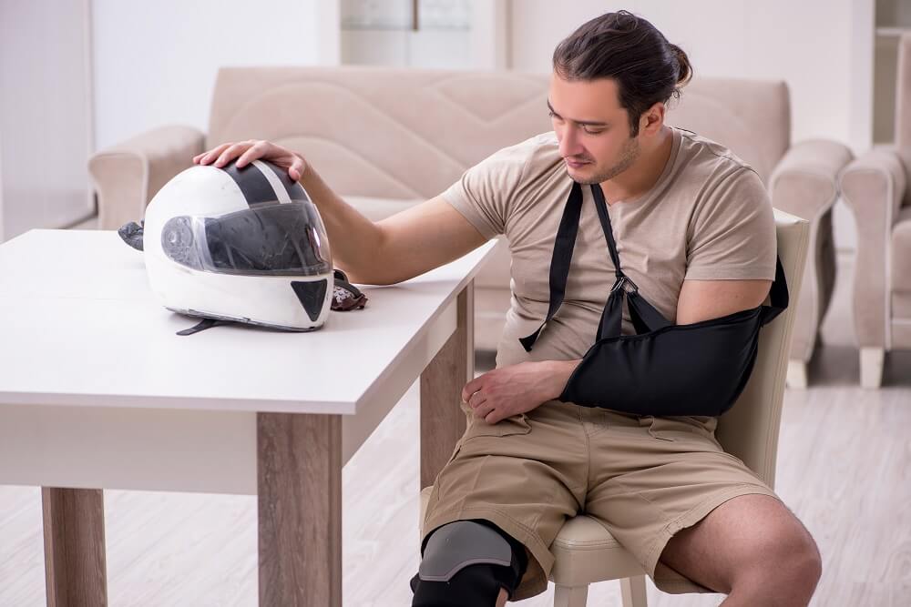 Sad injured motorcycle driver touching his helmet on the table.
